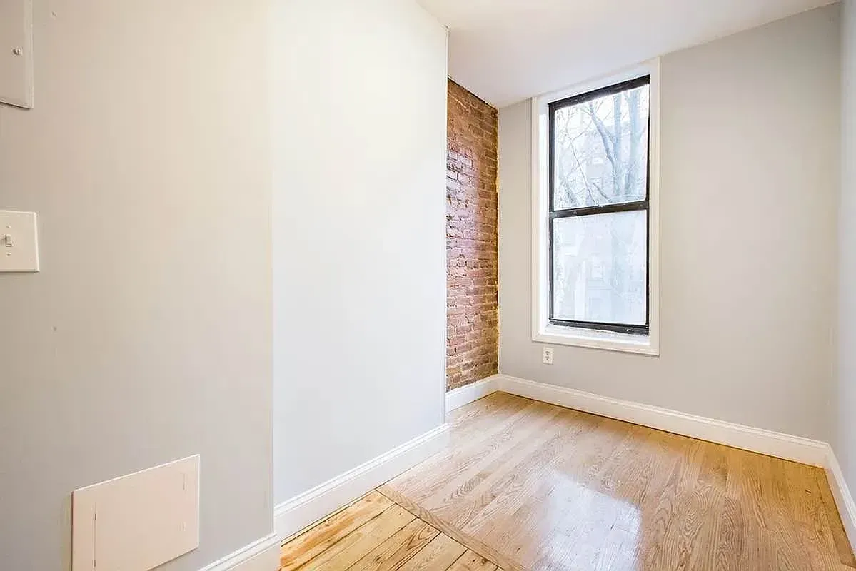 Three bedroom at 520 East 6th Street, empty bedroom with exposed brick and window