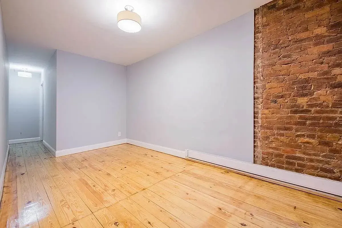 Three bedroom at 520 East 6th Street, empty room with exposed brick and wide-plank floors