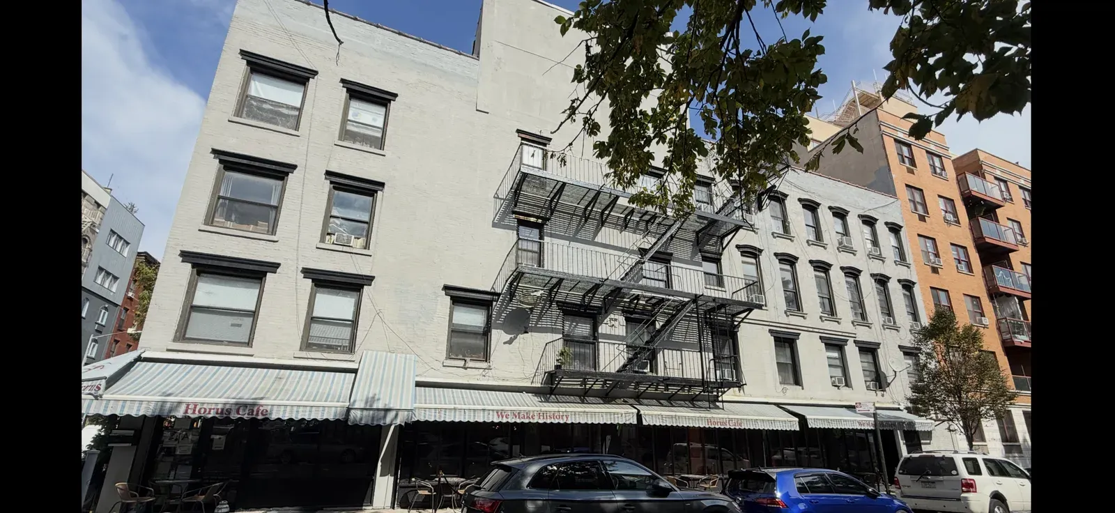 93 Avenue B, a corner walk-up with a fire escape and a cafe with awnings at street level