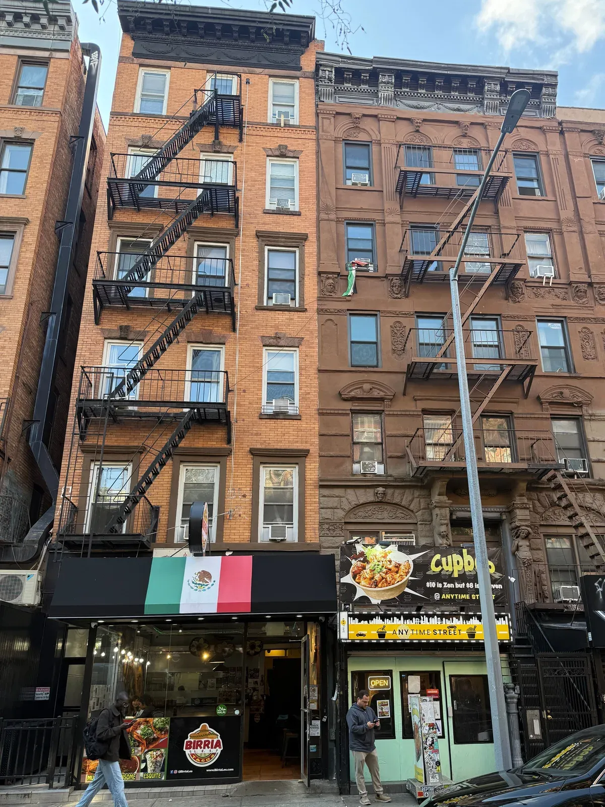 34½ Saint Marks Place, an orange brick walk-up with a fire escape and a restaurant at street level